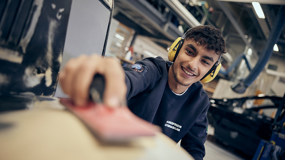 En elev med gula hörselskydd använder ett sandpapper.