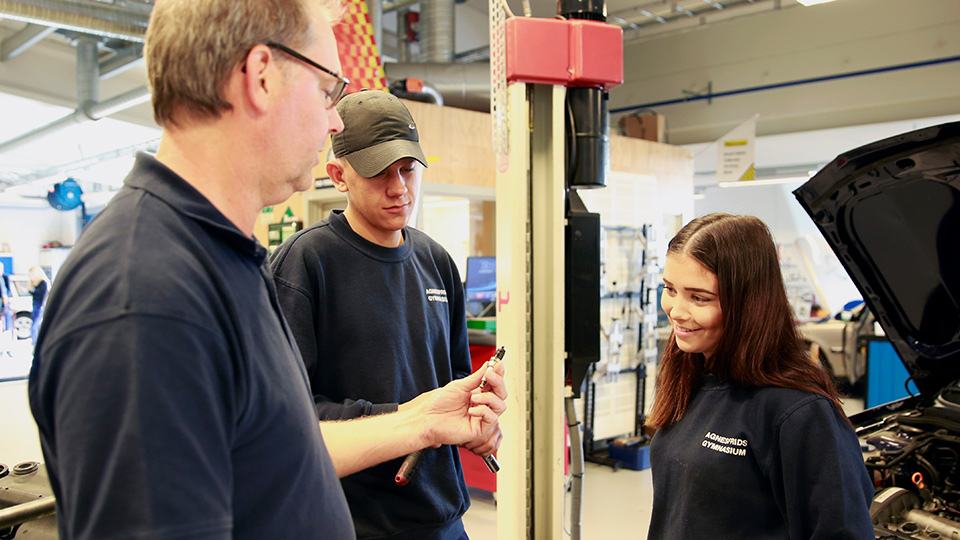 En lärare samtalar med två elever i peronbilsverkstaden