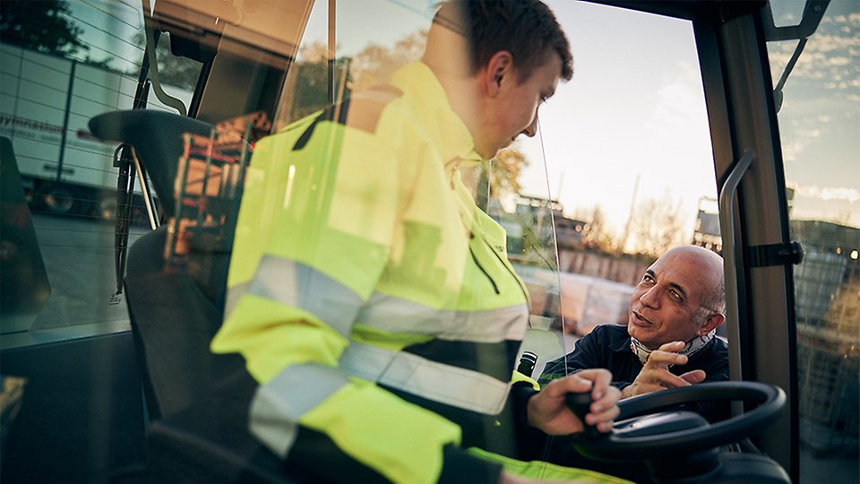 En lärare står utomhus och instruerar en elev som sitter i en truck