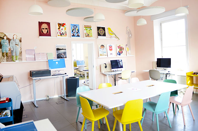 Rum med bord, kulörta stolar, Mac-datorer och affischer på väggarna.
