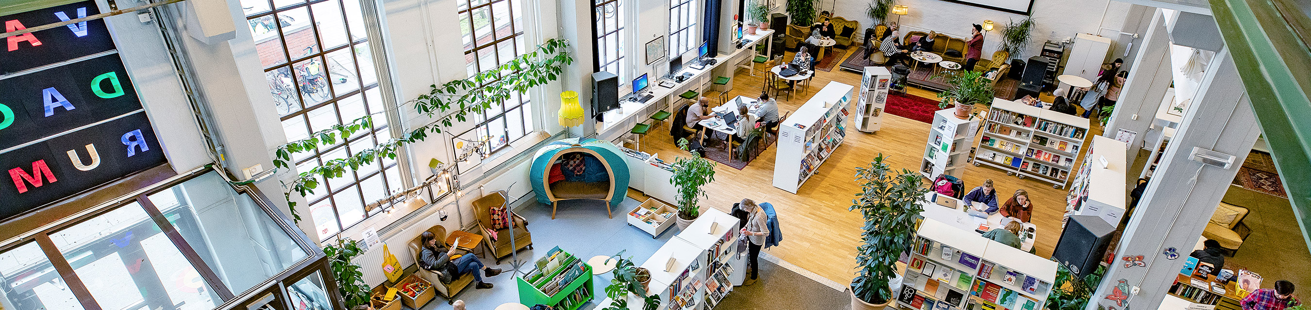 Interiör där man ser det stora luftiga biblioteksrummet på Garaget. Stora fönster, bokhyllor och sittplatser utmärker rummet.