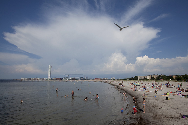 Strand med många badgäster. Ensam skyskrapa i bakgrunden.