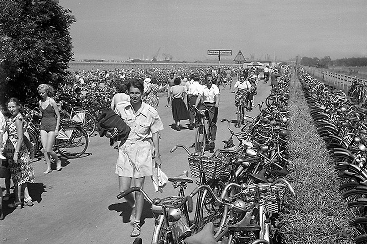 Äldre foto. Cykelbana vid havet. Många cyklar och sommarklädda fotgängare.